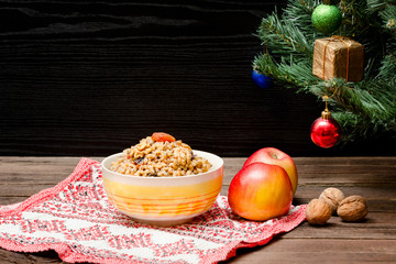 Dish of traditional Slavic treat on Christmas Eve. Christmas tree, apples, walnuts on a patterned tablecloth. Brown and blak wooden background.