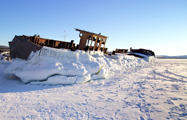 The abandoned old rusty ship placing on the coast of frozen lake. Baikal, Russia