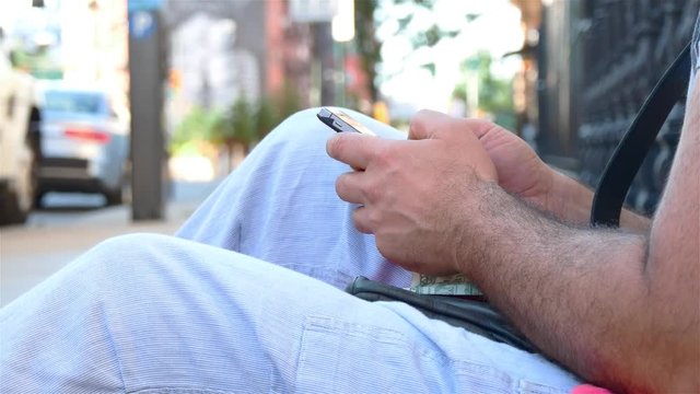 A man in a casual clothes is texting some message using a smartphone. City lifestyle on the background.