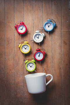 White cup on lying on side with colored alarm clocks