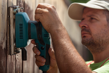 Worker using a vibrating sander on a wooden fence