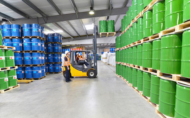 Arbeiter in einem Warenlager für Chemiekalien lagern Fässer // Workers in logistics