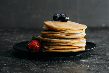 stack of pancakes with blueberries and strawberry on black plate