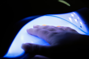 Closeup of the hand of a woman inside a UV or LED lamp, curing her recently applied gel nail polish at a salon