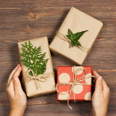 Gifts packed in a minimalistic style and child's hands on a wooden background. The concept of stylish, minimalistic holidays, hipsters, trends, New Year, Christmas, birthday, etc.