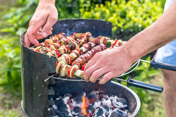 Man grilling skewers on barbecue grill with charcoal and smoke, outdoor bbq with colorful grilled food, close-up of various meat and vegetables