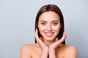 Close up portrait of cute joyful pretty young woman with excellent skin and beaming smile, she is admiring her beauty in a mirror, isolated on grey background, copyspace