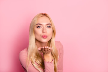 Close up portrait of young pretty woman sending kiss to the camera, standing over pink background