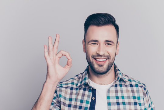 Close up portrait of attractive, smiling man in checkered shirt with bristle showing ok sign over grey background