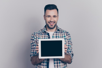 Portrait with copy space of young, smiling, cheerful man showing black tablet screen, presenting a gift, present, using, choosing modern electronic device, standing over grey background