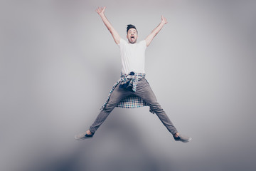 Happiness, freedom, motion and people concept - happy  attractive handsome young man with bristle jumping in air like star with raised hands and opened legs, showing tongue over grey background