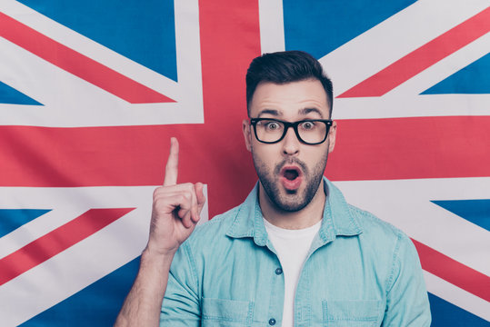 Portrait of handsome attractive guy with stubble in glasses showing index finger up, find a solution, have an idea with opened mouth over English flag background