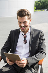 Male businessman or worker in black suit with tablet sitting on chair