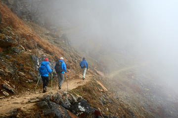 Group Hikers with Backpacks walking down on Mountain Trail in foggy mountains.