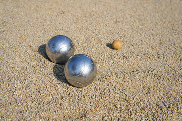 The silver petanque ball is placed between the wooden jack balls on the sandy petanque court.