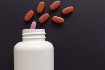 All tablets are red except one: pink. Capsules spilling out of white bottle.