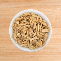 Top view of slivered almonds in a small white bowl on a wood table.