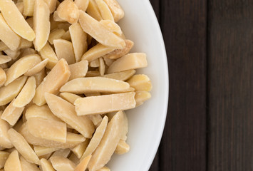 Top close view of slivered almonds in a small white bowl atop a brown wood place mat.