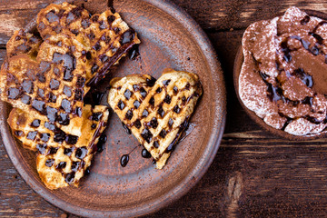Belgian heart shaped waffle  on brown plate, with hot chocolate with marshmallow on wooden background.