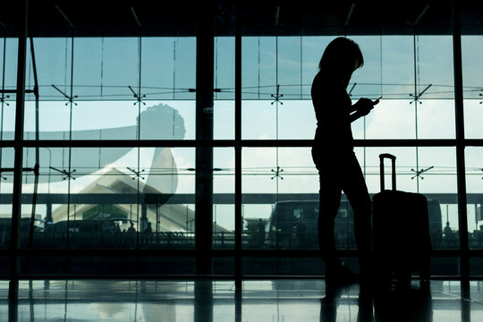 silhouette of girl with luggage stand near window in airport