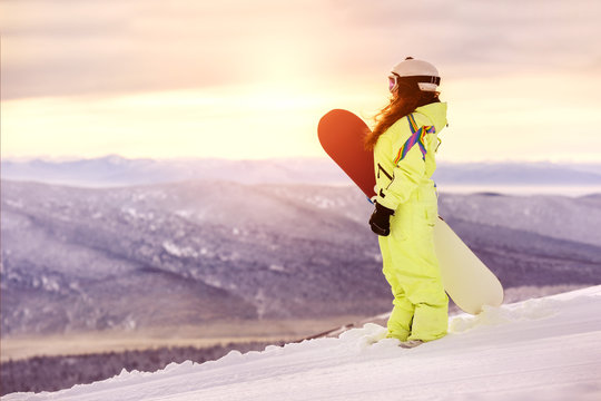 Young girl with snowboard at ski clope at sunrise