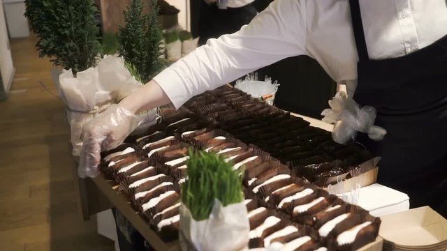 The waiter places eclairs and profiteroles on a buffet table with desserts.