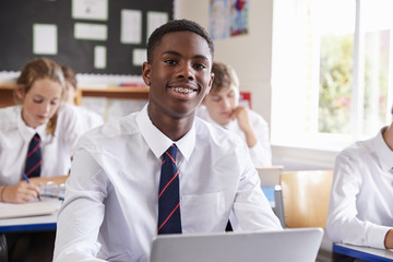 Portrait Of Male Pupil In Uniform Using Laptop In Classroom