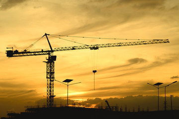Evening silhouette of tower crane at construction of residential buildings and large shopping malls. Indicates economic growth.