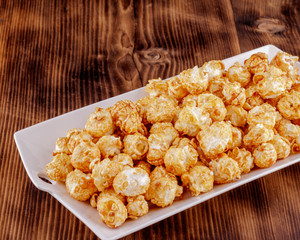 Popcorn with caramel on a white ceramic dish on wooden background