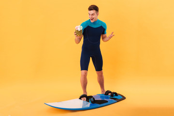 Full length image of Surprised happy surfer in wetsuit