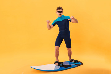 Cheerful surfer in wetsuit and sunglasses using surfboard