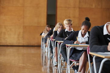 Teenage Students In Uniform Sitting Examination In School Hall - obrazy, fototapety, plakaty
