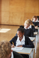 Teenage Students In Uniform Sitting Examination In School Hall - obrazy, fototapety, plakaty