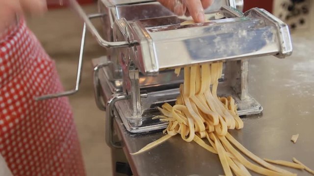 Making spaghetti with a traditional style pasta machine. Cooking process close up. Chef use pasta cutting machine.