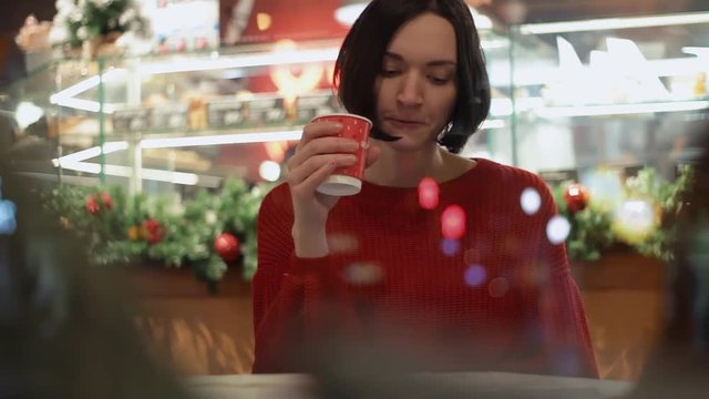 Portrait of young attractive woman using smartphone sitting in cafe. Xmas time