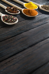 different spices in wooden spoons on a black wooden background