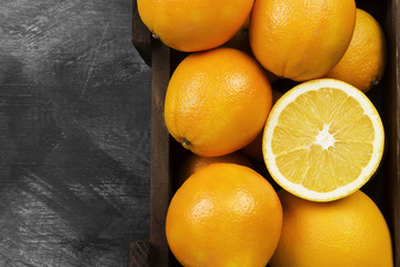 Oranges in a wooden box on a black background. Top view, copy space. Food background