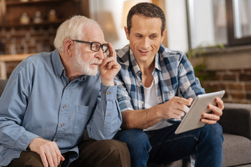 Look here. Pleasant young man pointing at the tablet, showing an interesting article to his elderly...