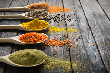 different spices in wooden spoons on a black wooden background