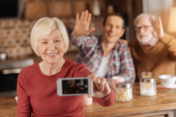Collecting happy moments. Pleasant senior woman taking a selfie of herself and her husband and son while they having breakfast in the kitchen