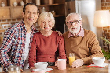 Calm Sunday morning. Pleasant happy family sitting in the kitchen, having breakfast and posing for the camera, smiling at the camera