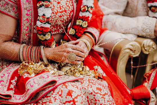 Stunning Indian bride dressed in Hindu traditional wedding clothes lehenga embroidered with gold and a veil during Saptapadi ceremony holds golden accessories on her knees