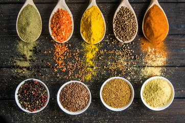 different spices in wooden spoons on a black wooden background