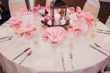 Wedding dinner table decorated with pink flowers, napkins and wooden lantern
