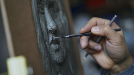 Close-up of Sculptor creating sculpture of human's face on canvas in art studio