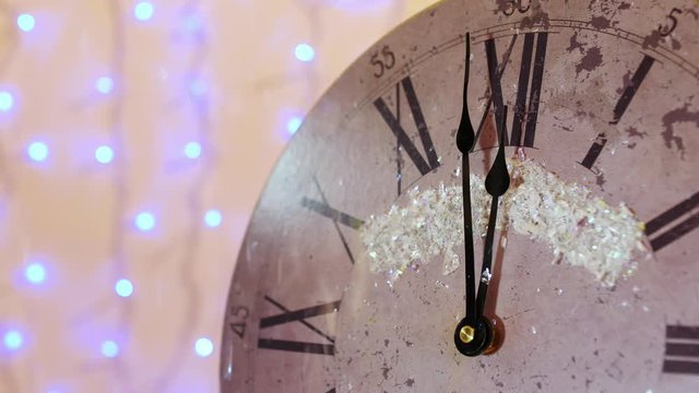 A close-up of the New Year's clock and snow falling with luminous lanterns in the background. Abstract blurred christmas lights bokeh background. Almost at 00 oclock