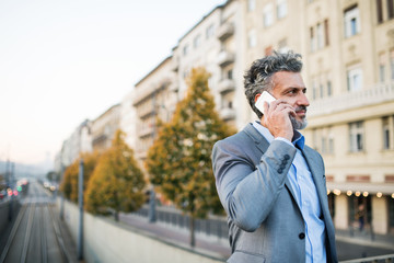 Mature businessman with a smartphone in a city.