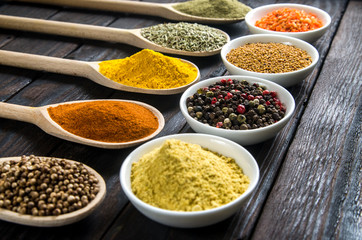 different spices in wooden spoons on a black wooden background