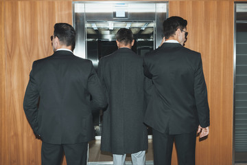 Back view of bodyguards and businessman standing at elevator