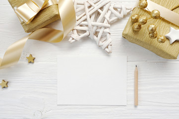 Mockup Christmas greeting card with gold gift ribbon, flatlay on a white wooden background, with place for your text